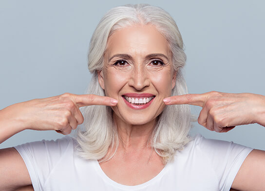 woman pointing to her bright, white smile